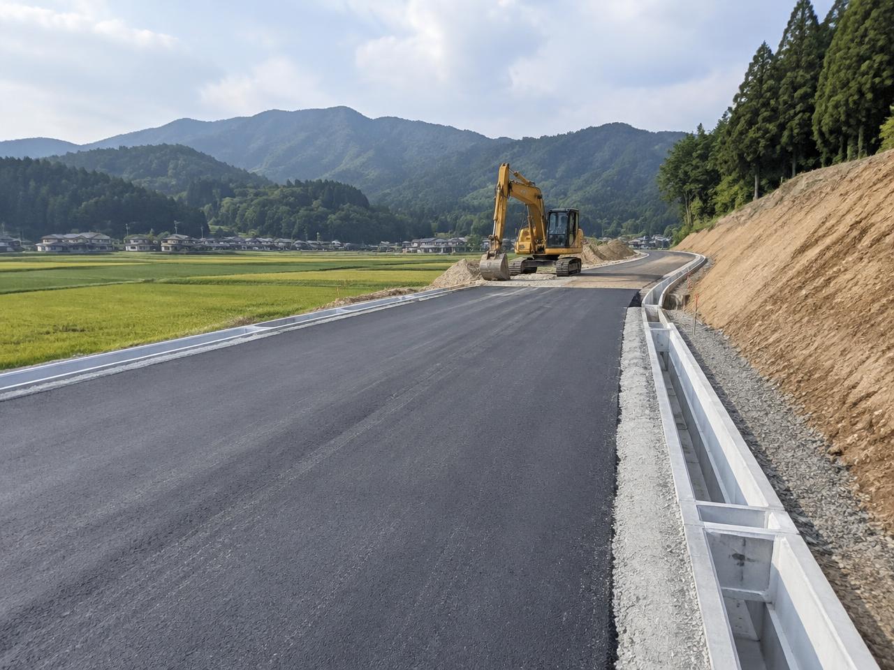 舗装を終えた道路と側溝、造成中の法面が並ぶ土木工事の現場